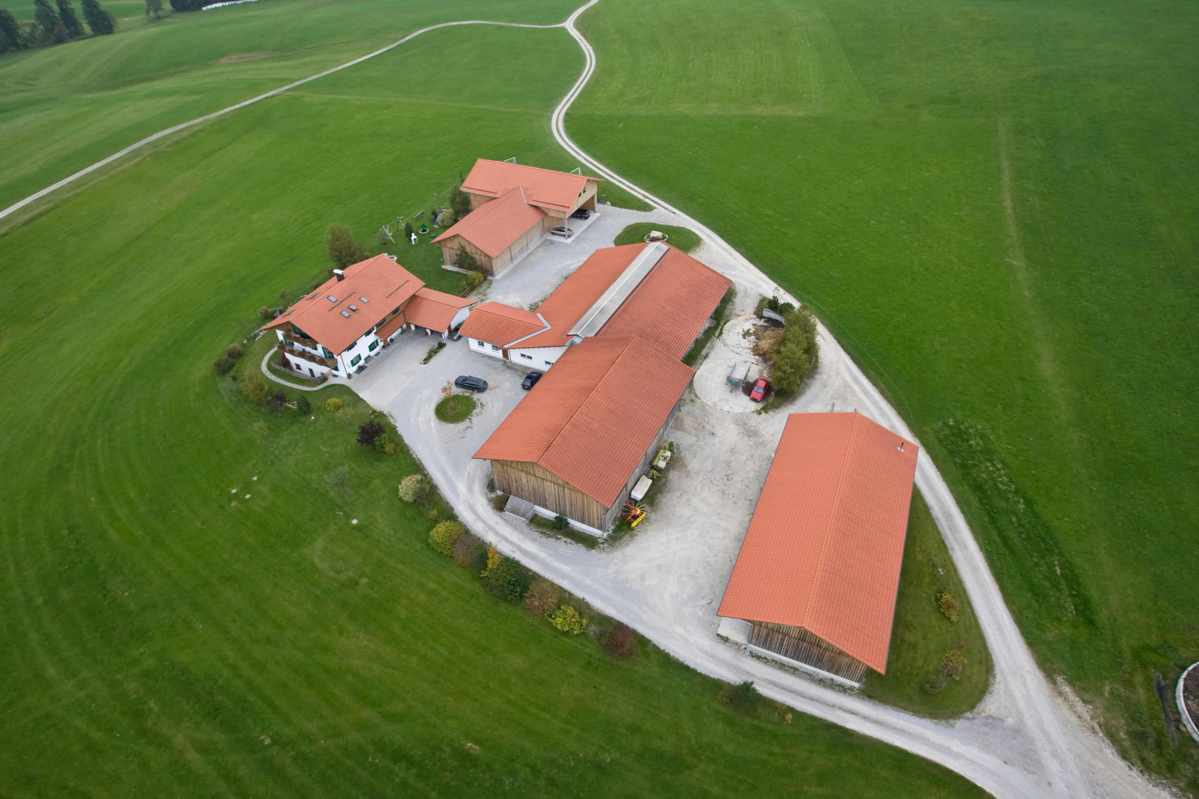 Luftbild eines Hofs mit Wohnhaus und Stallgebäuden zwischen Wiesen