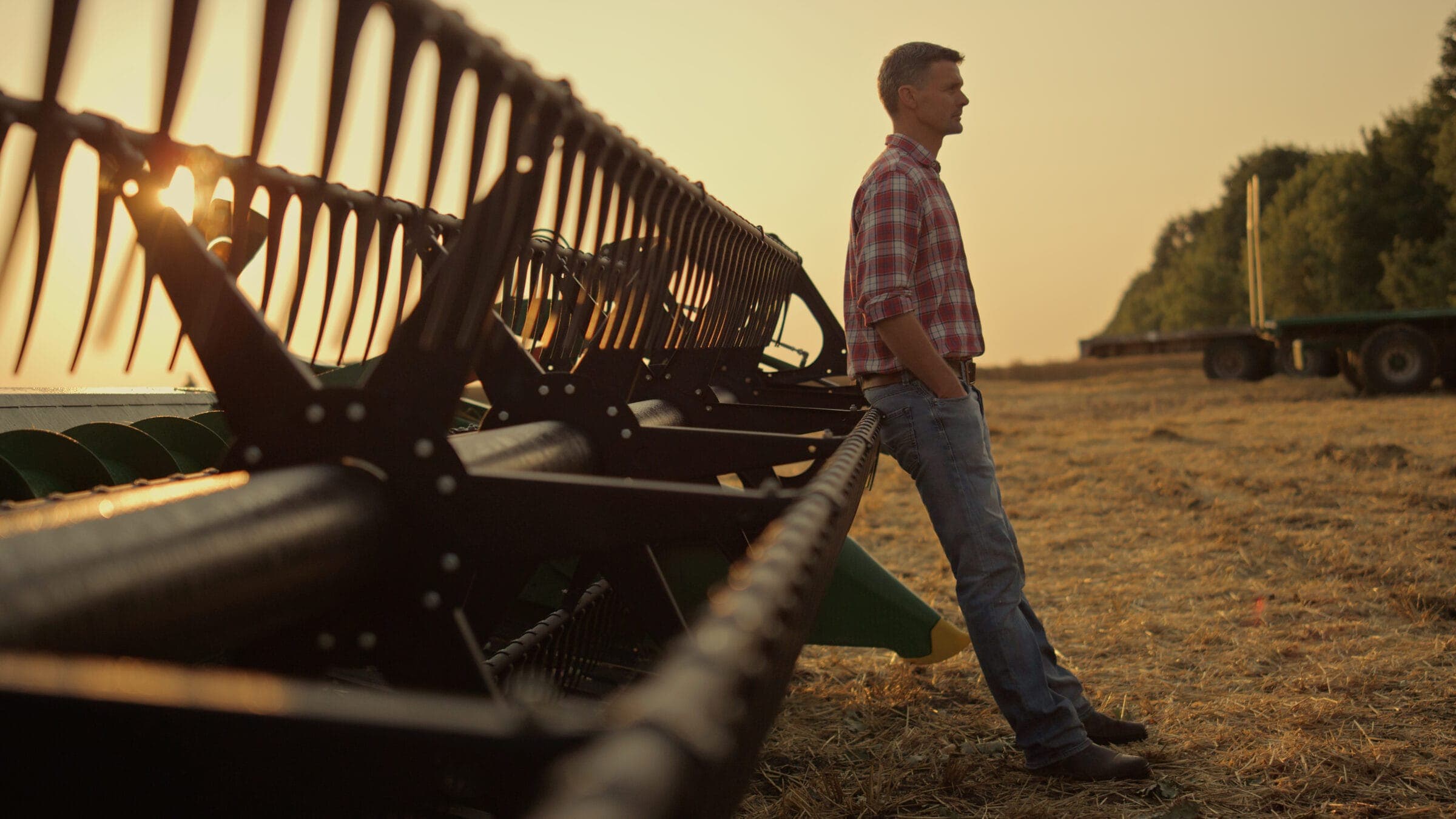 Landwirt neben dem Schneidwerk eines Mähdreschers bei Sonnenuntergang
